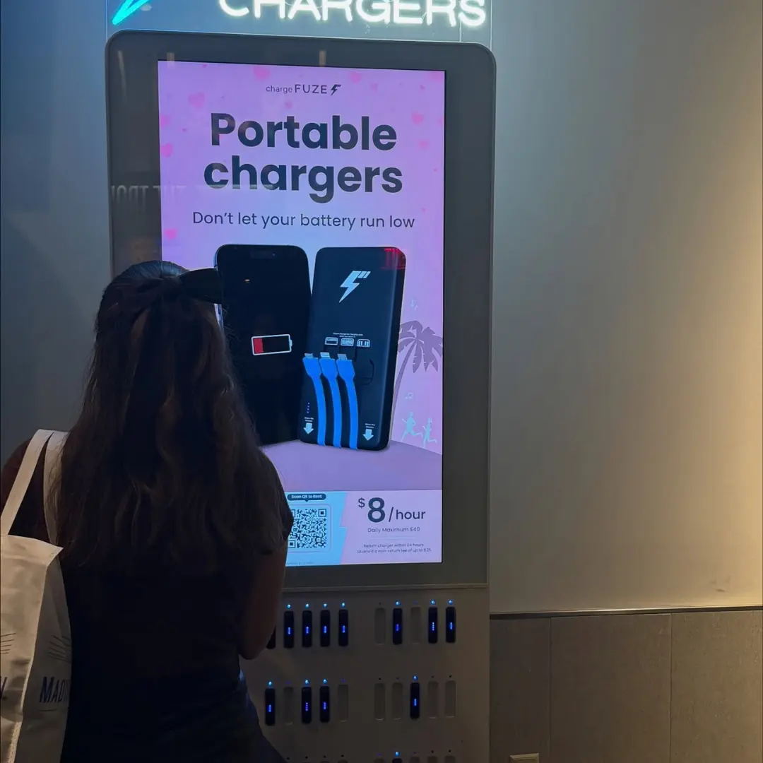 Travel-friendly charging options at a ChargeFUZE kiosk offering portable charger rentals for $8 per hour as a woman browses the screen