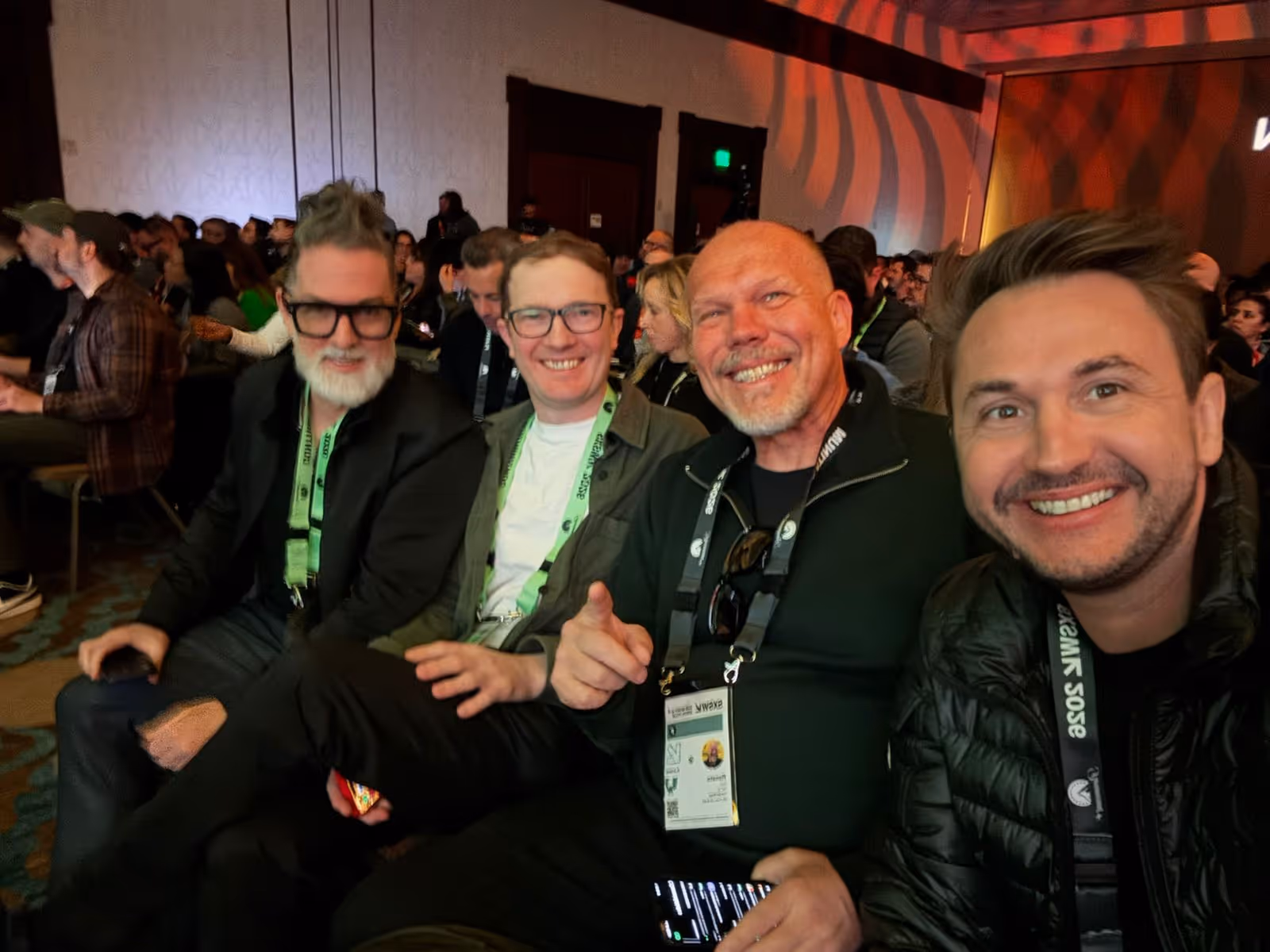 Quatro homens sorrindo sentados lado a lado no SXSW 2026 com crachás pendurados no pescoço.