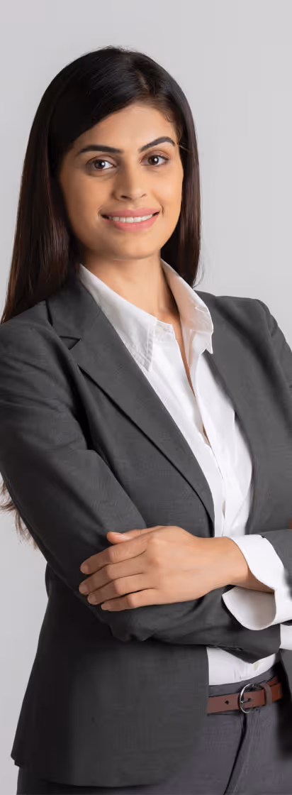 A confident young woman in a grey suit, smiling with arms crossed, posed in front of a light grey background.