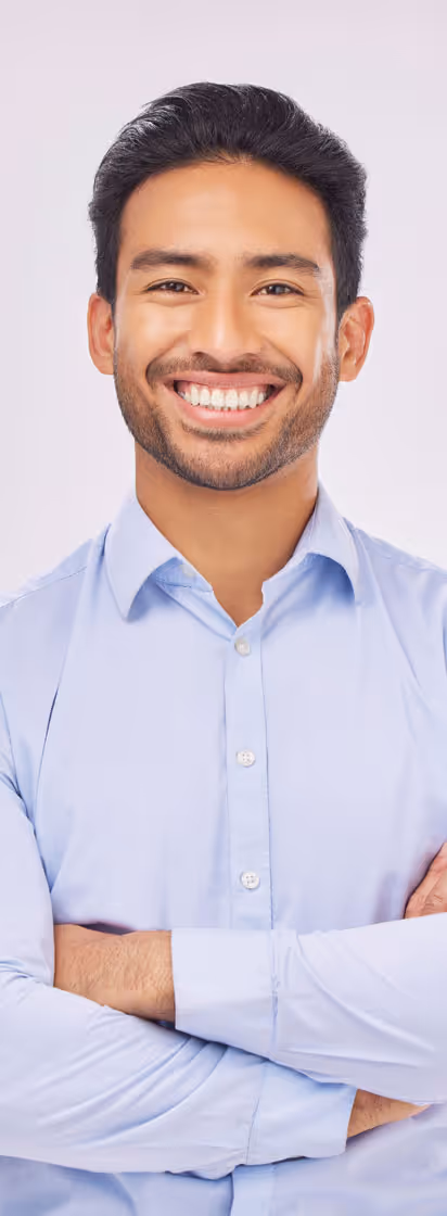 A smiling young man in a light blue shirt standing confidently with arms crossed against a light background.