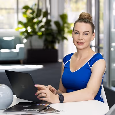 Rachael Greaves, CEO in a blue dress working on a laptop in a modern office