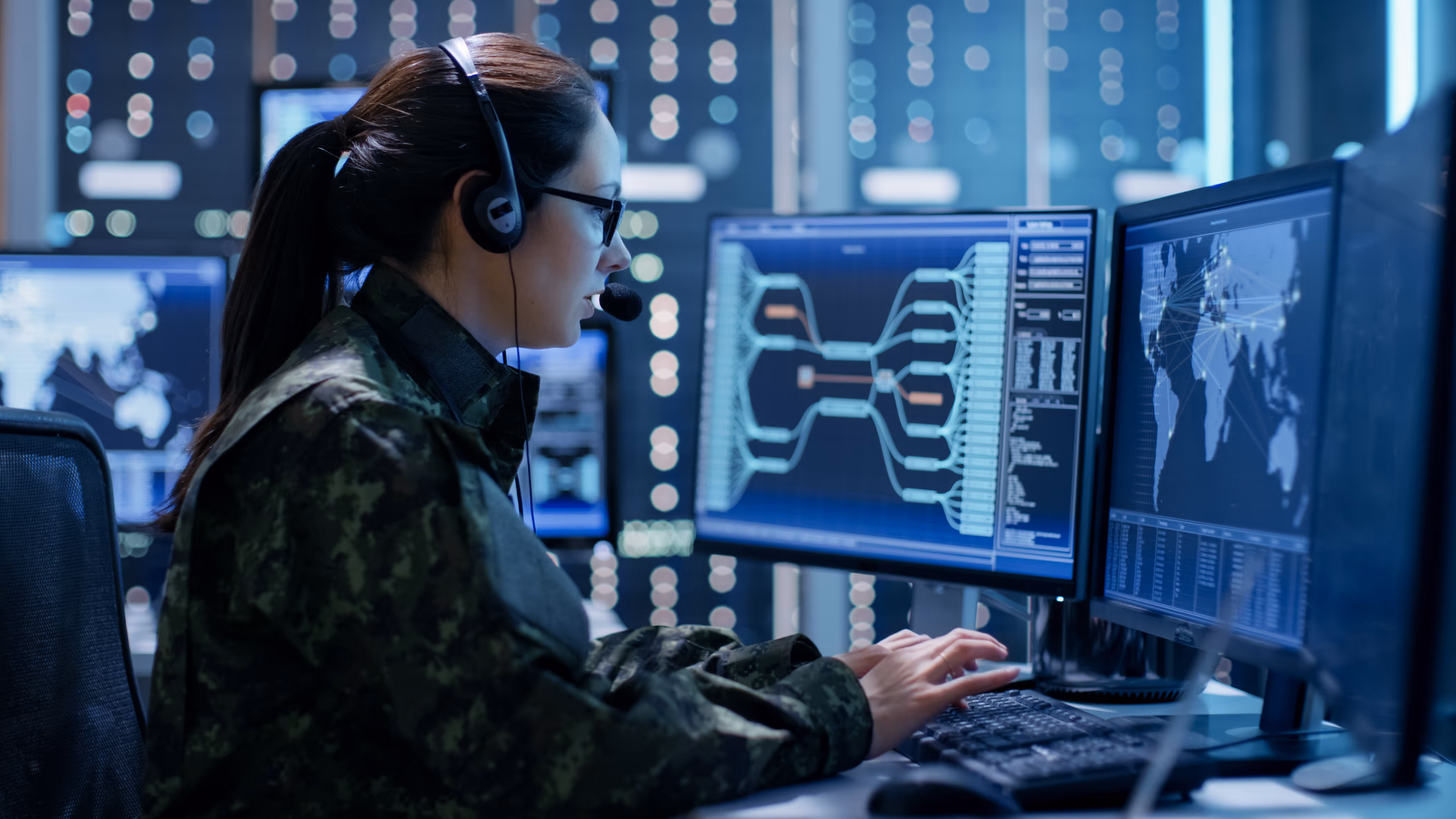 Female military officer using multiple monitors to monitor security operations in a data center.