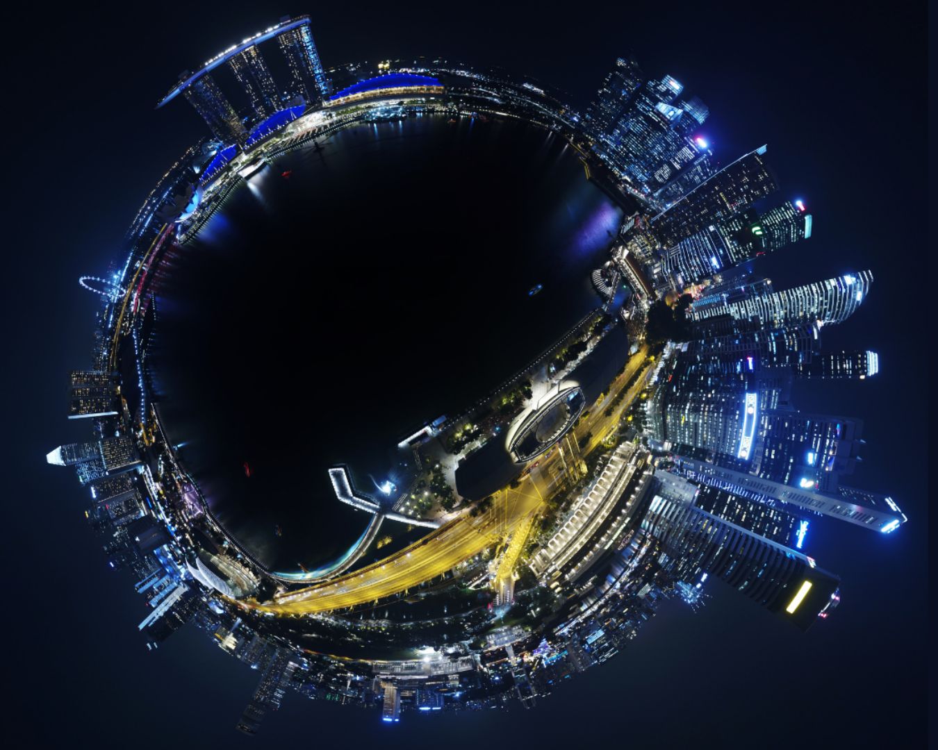A group of young professionals, sitting around a table, smiling and discussing work in a casual, collaborative environment. One person is holding a tablet, while others have laptops and cups of coffee in hand, emphasising teamwork and a relaxed setting.