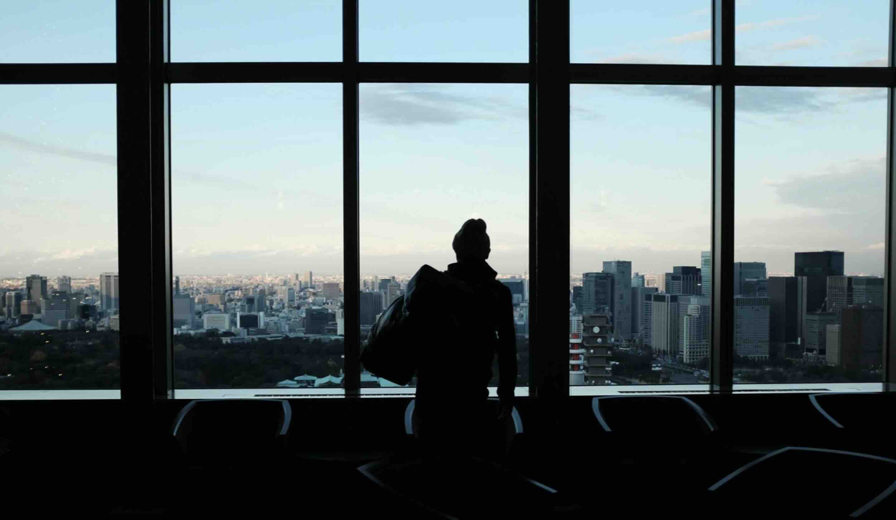 A traveler looks out at a city skyline through airport windows