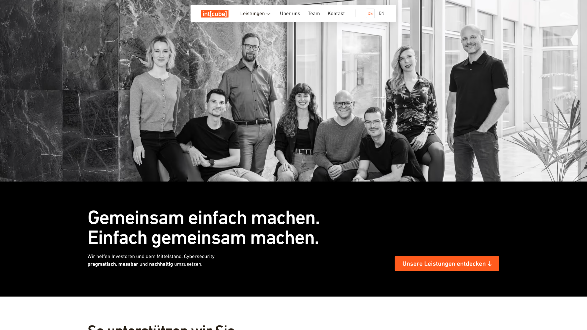 Gruppenporträt von acht lächelnden Personen, vier sitzend und vier stehend, in einem modernen Büro mit großen Fenstern und Marmorwänden.