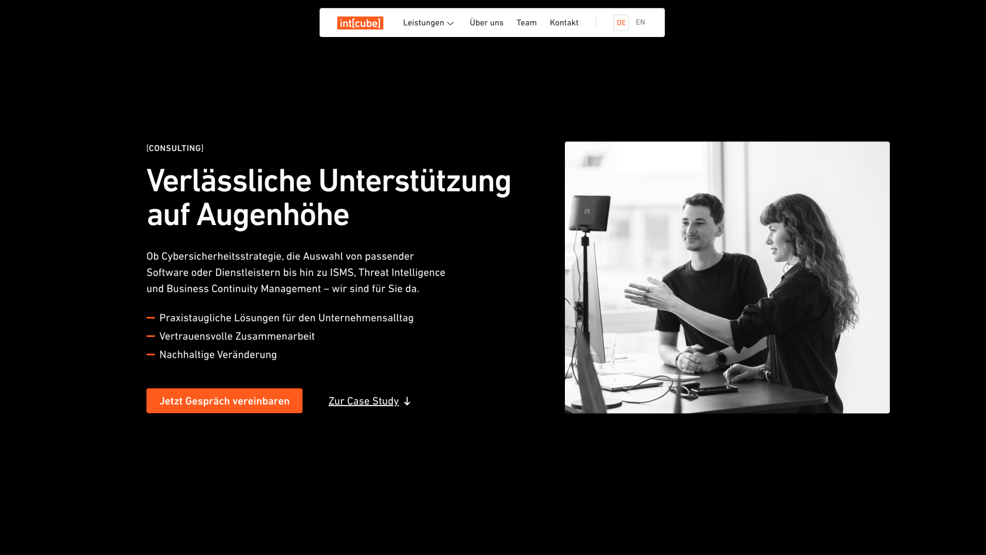 Schwarzweiß Foto eines Mannes und einer Frau, die sich vor einem Computermonitor in einem hellen Büro austauschen.
