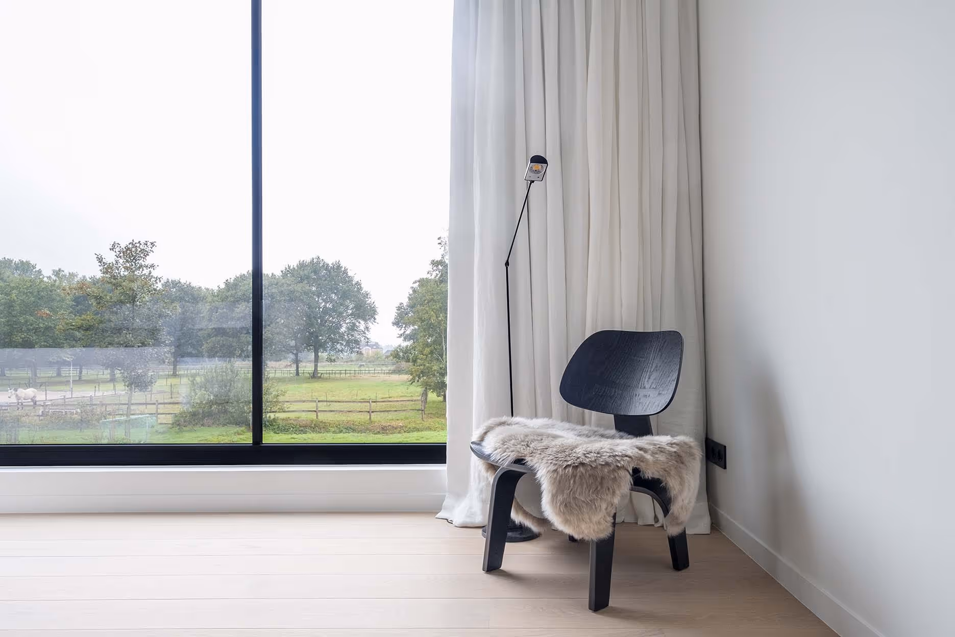 Eigentijdse hoek met stoel en schapenvacht voor groot raam met uitzicht