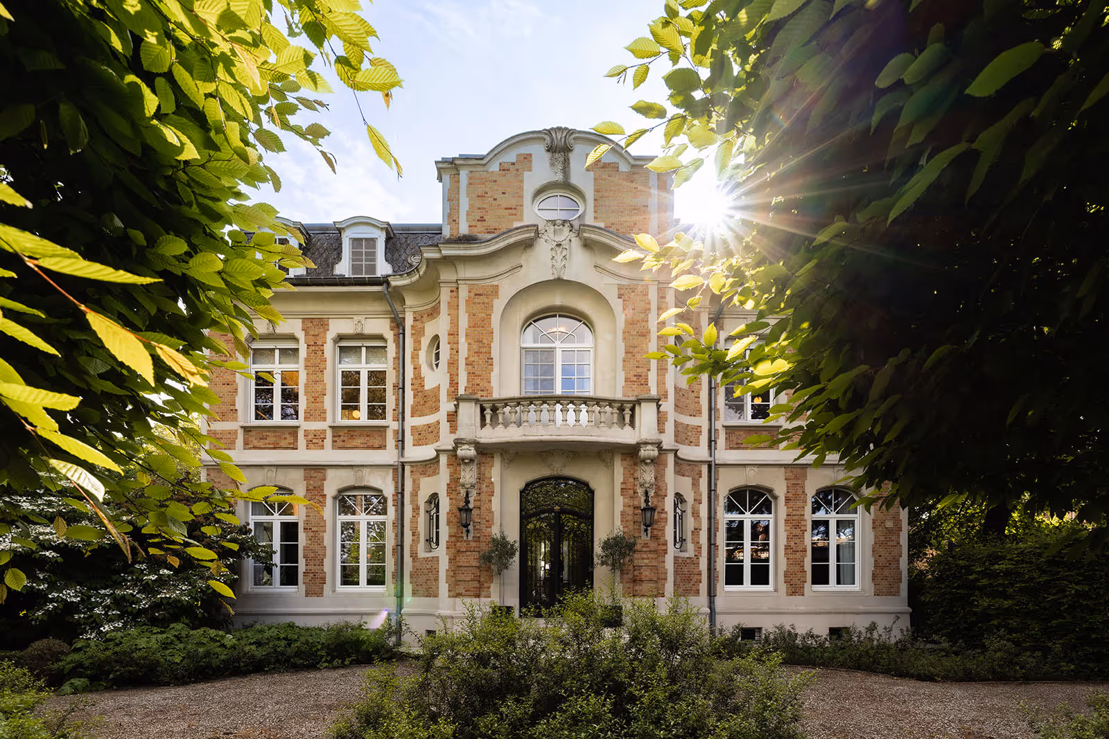 Historisch herenhuis omgeven door bomen met zonnestralen die door het bladerdak schijnen
