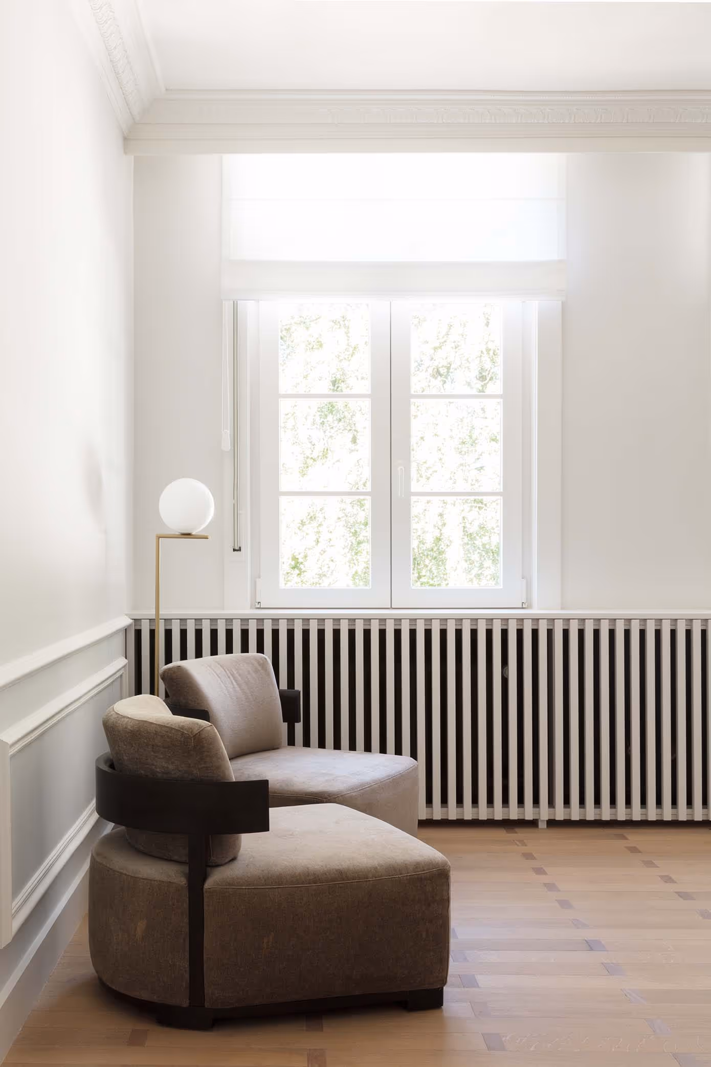 Comfortabele bruine loungestoel bij een raam met witte gordijnen en gestreepte radiatorombouw in een heldere kamer