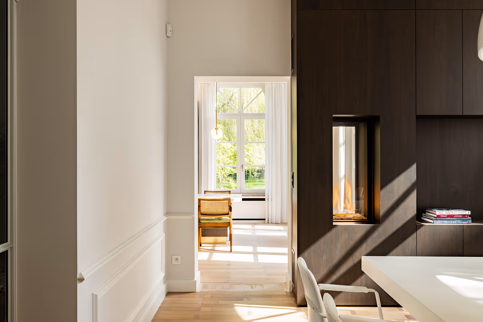 Zonovergoten interieur met een houten stoel bij het raam en een ingebouwde moderne haard in een donkere wand