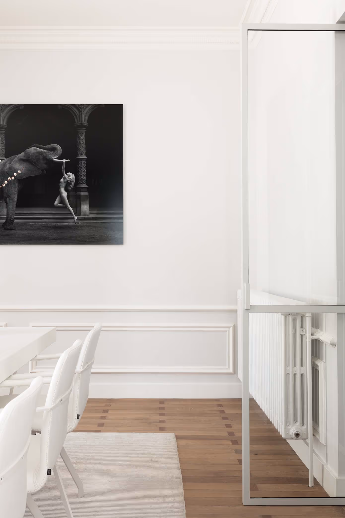 Moderne eetkamer met witte stoelen en een zwart-witte foto van een olifant en danser aan de muur