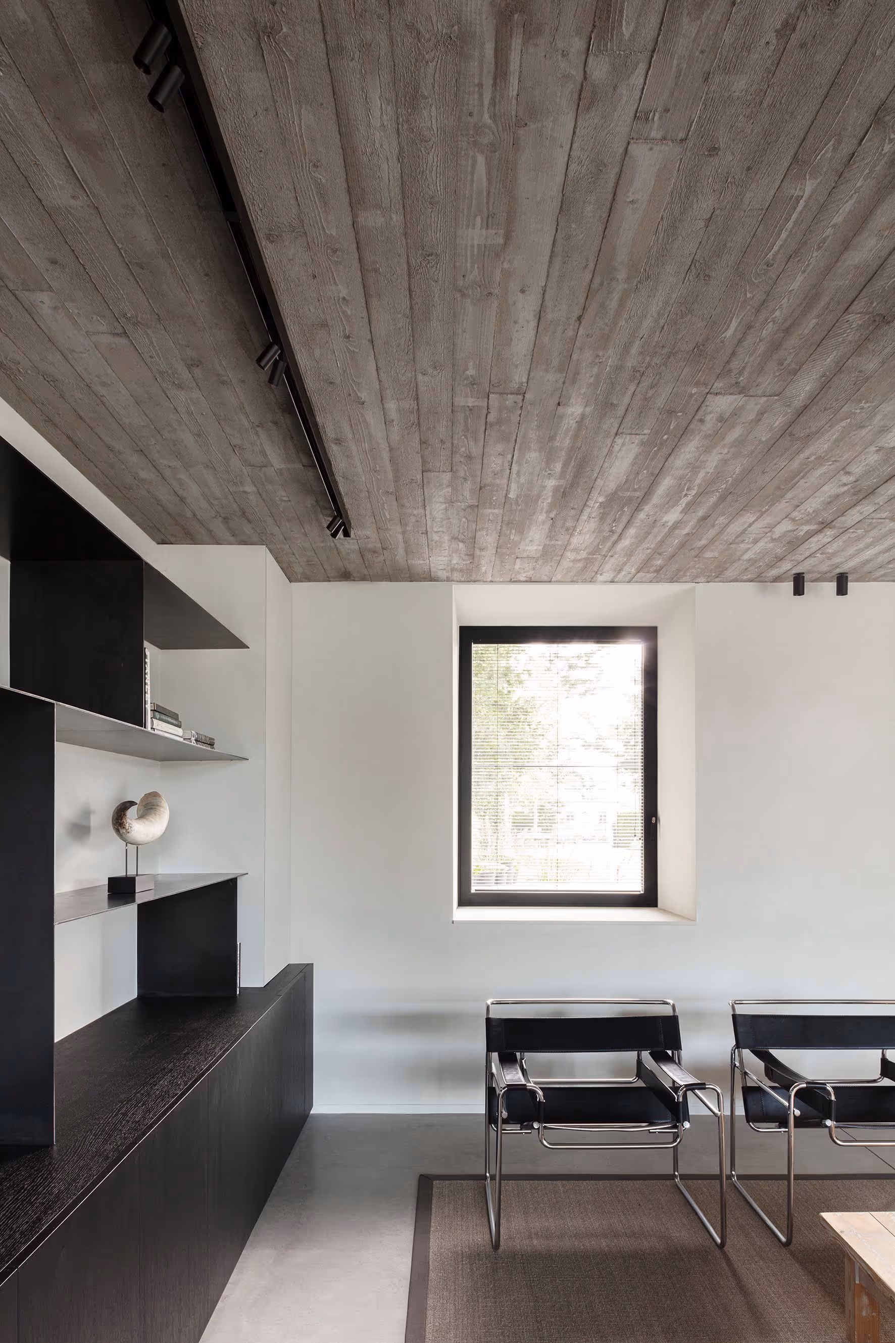 Moderne leefruimte met strakke zwarte rekken, betonnen plafond en een groot raam.