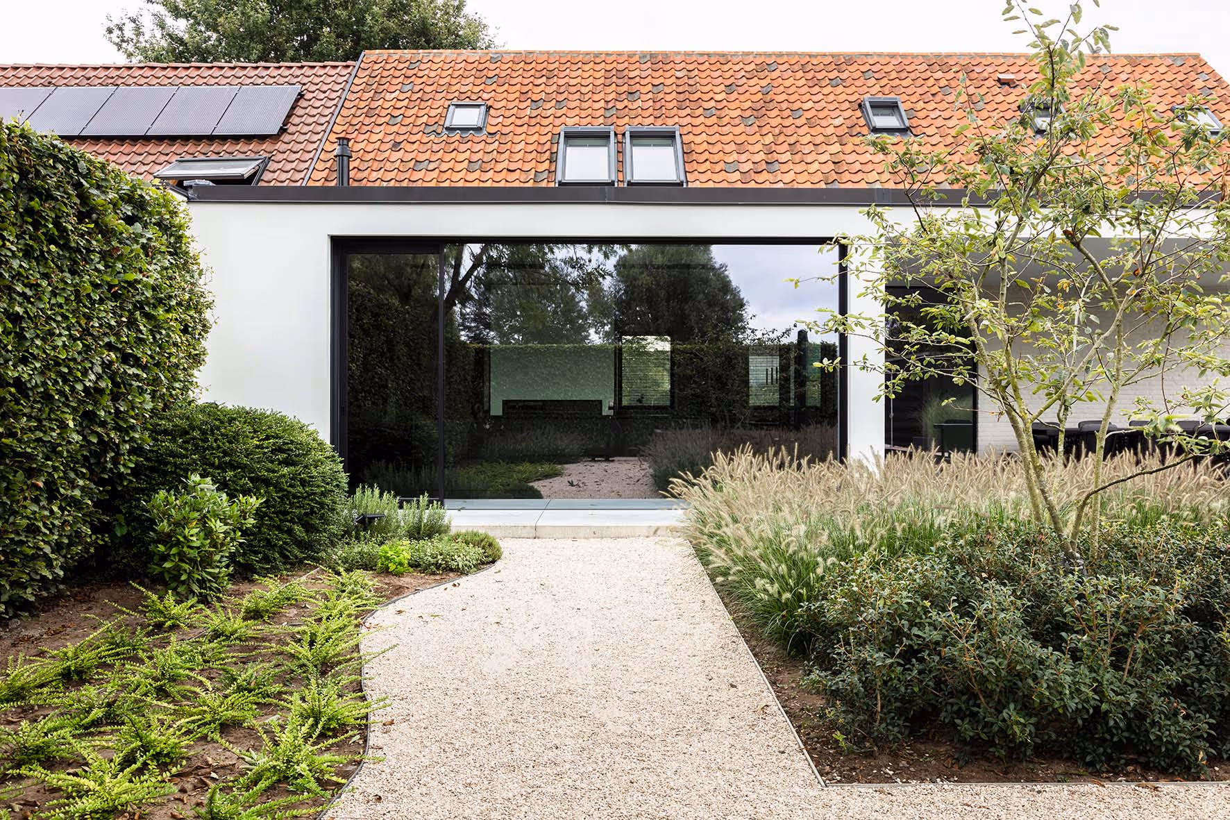Vooraanzicht van een modern huis met een naadloze overgang naar de aangelegde tuin en centraal gelegen zwembad
