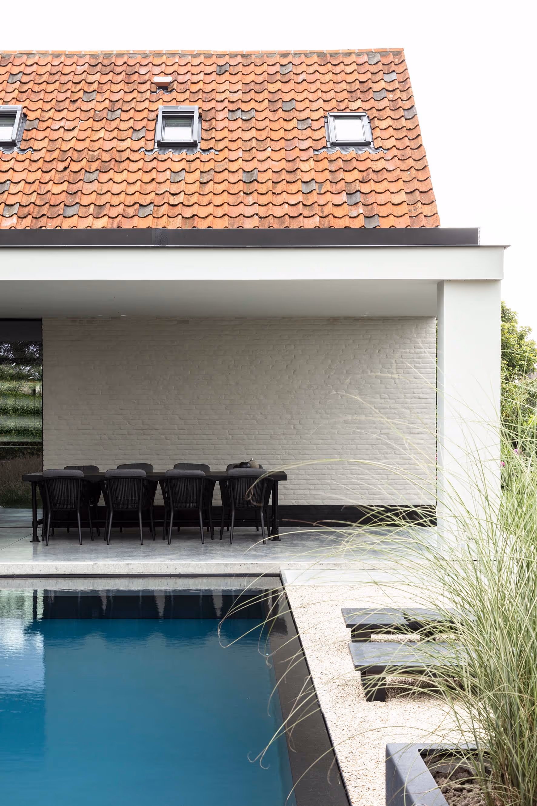 Chique buiteneetruimte onder een uitgebreide luifel met zicht op een gestructureerd zwembad en een klassiek dak