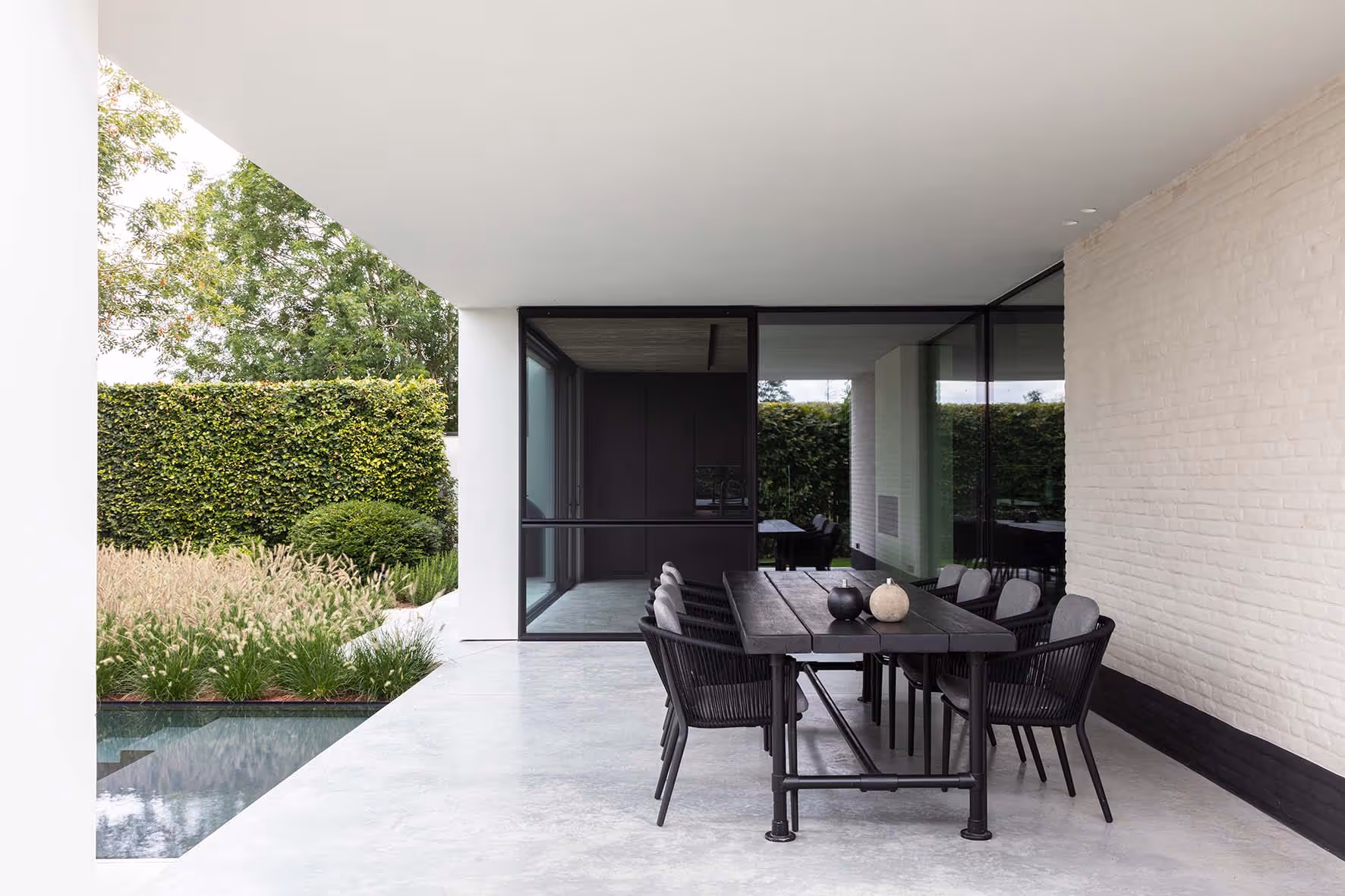 Moderne buiten eethoek met zwarte stoelen en tafel naast een reflecterend zwembad omringd door weelderige planten
