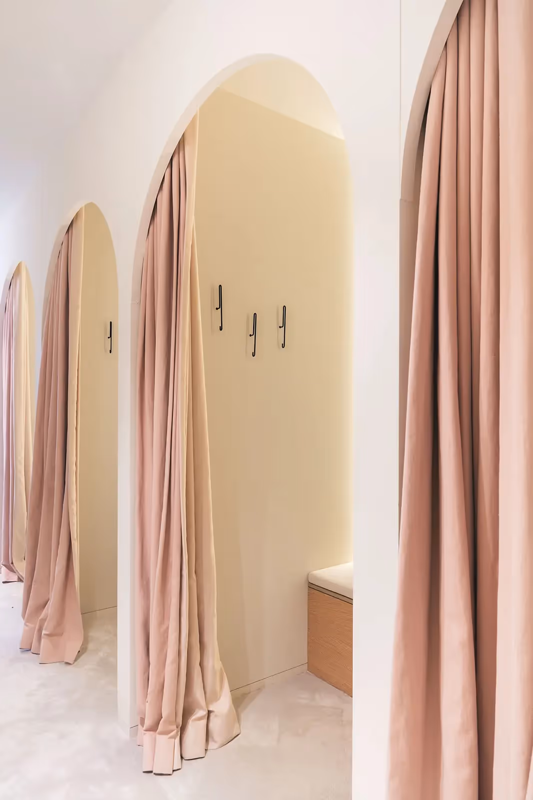 Moderne winkelinterieur met boogvormige paskamers en zachtroze gordijnen.