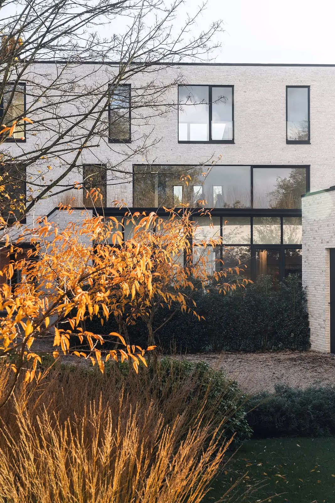 Modern huis met grote glazen gevel en herfstgebladerte.