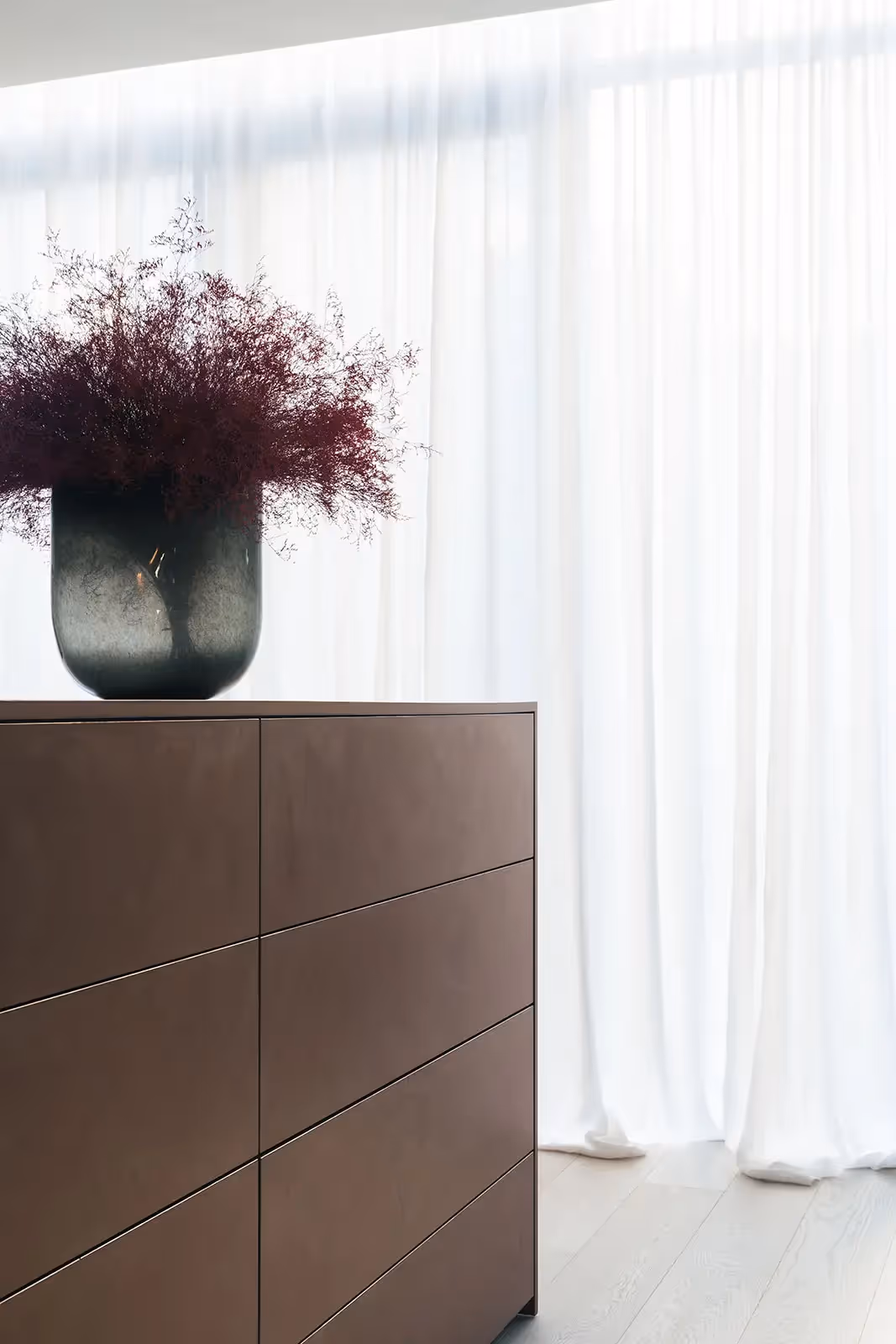 Stijlvol interieurdetail met bruine ladekast en grote vaas met paarse plant.