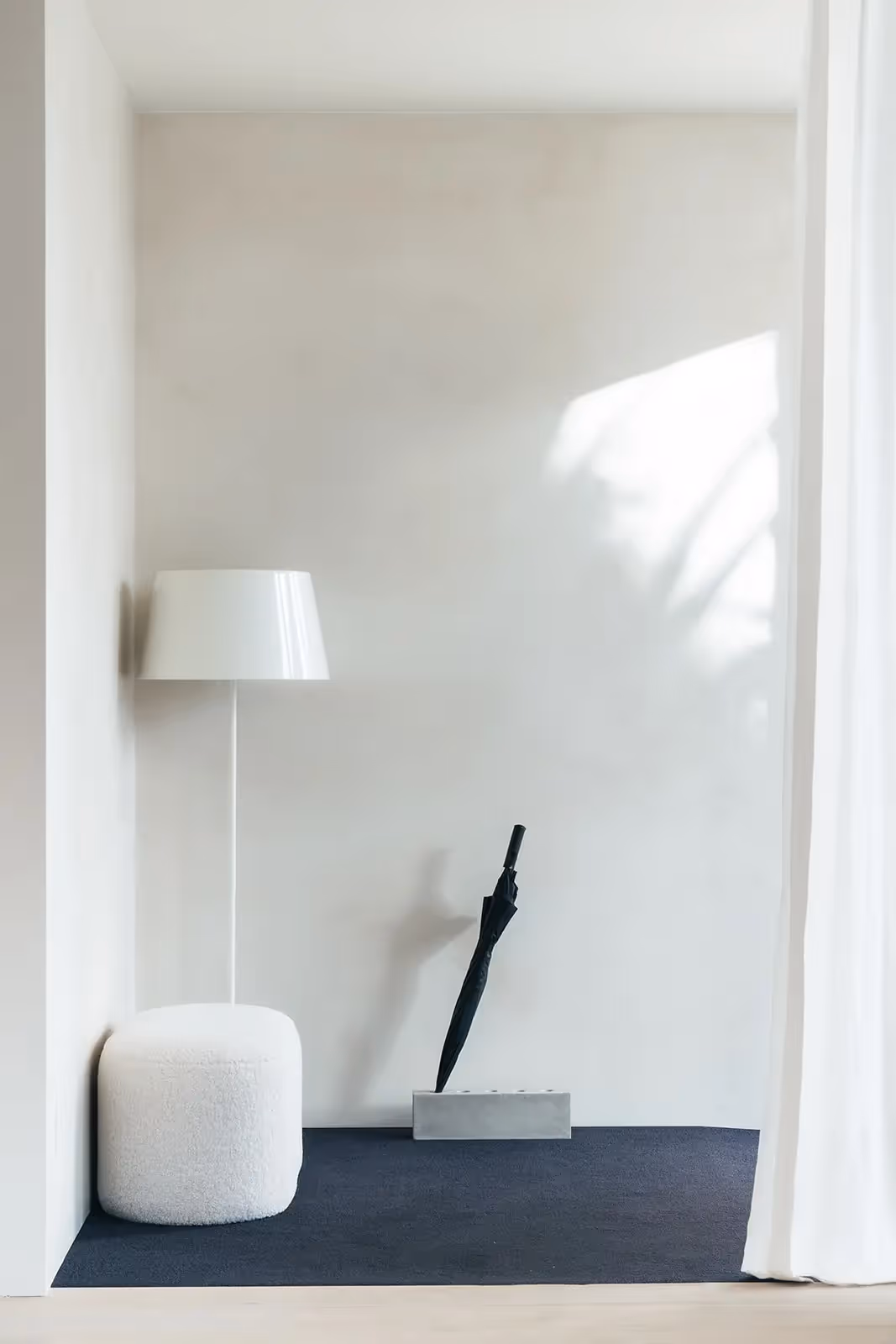 Minimalistische hoek met een artistiek beeld, ronde lamp en poef.