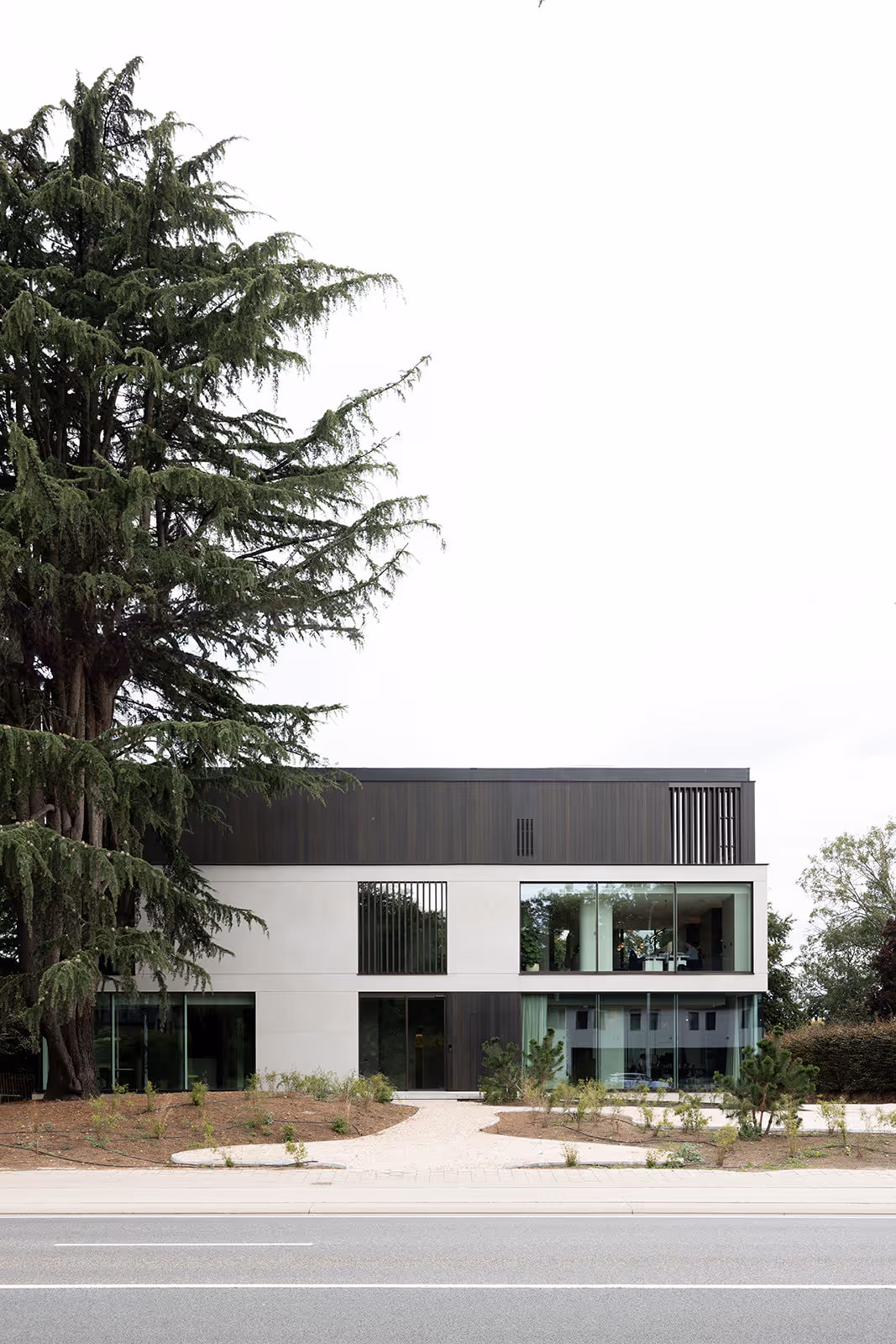 Stijlvol kantoorgebouw met betonnen en houten gevel, omgeven door weelderig groen en kiezelstenen pad.
