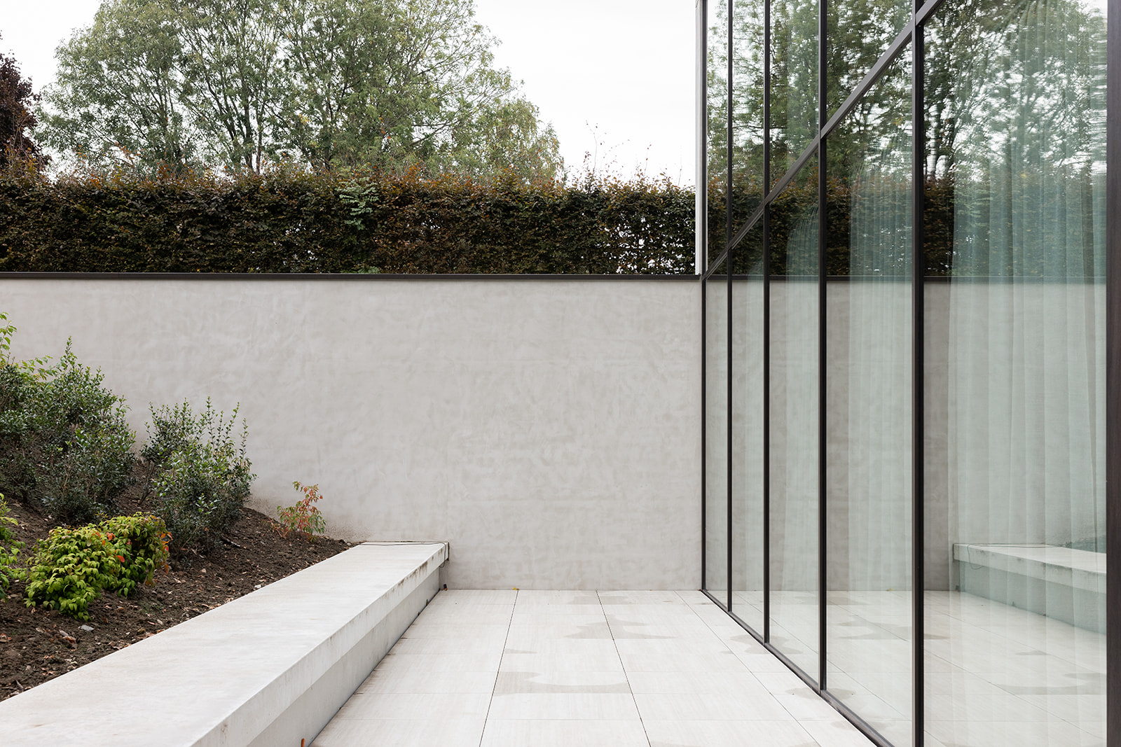 Stijlvol kantoorgebouw met betonnen en houten gevel, omgeven door weelderig groen en kiezelstenen pad.