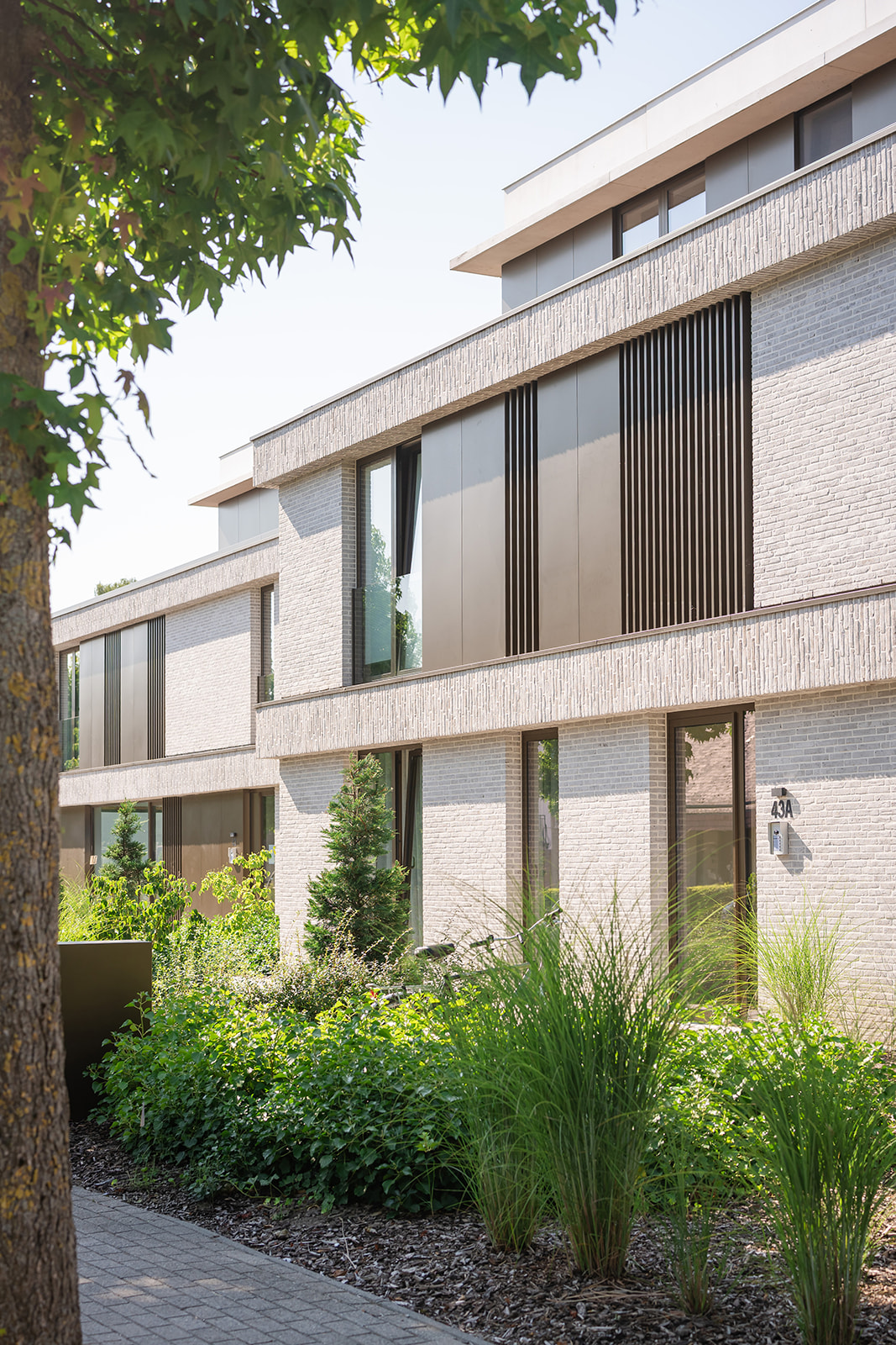 Ruime tuin voor een modern appartementencomplex met een persoon zittend op een bankje genietend van het zonnige weer.