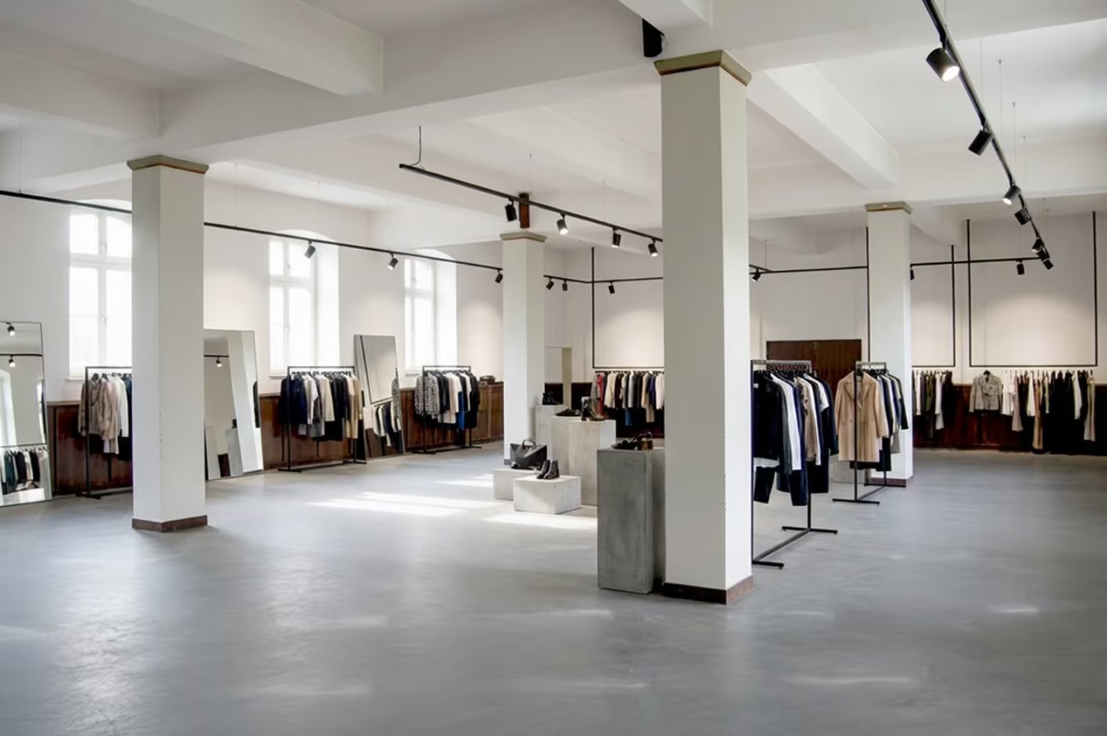 Der Raum als Showroom: Kleiderstangen und Podeste zwischen weißen Säulen auf hellem Estrichboden