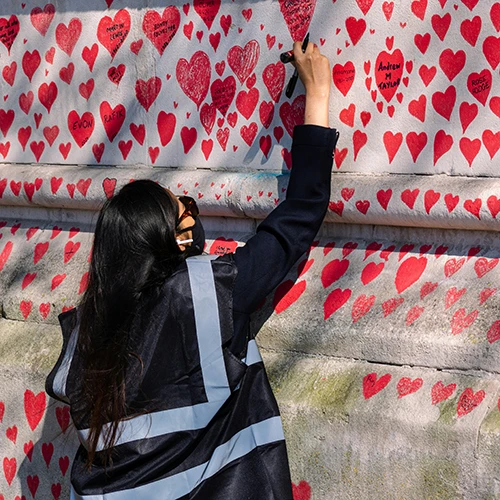 A girl drawing red hearts with messages on a wall full of them