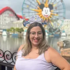 Smiling woman wearing Mickey Mouse ears with a colorful amusement park ferris wheel in the background.