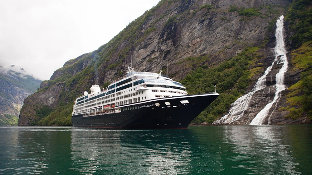 An Azamara Cruise Ship sailing next to a hill on a winter day