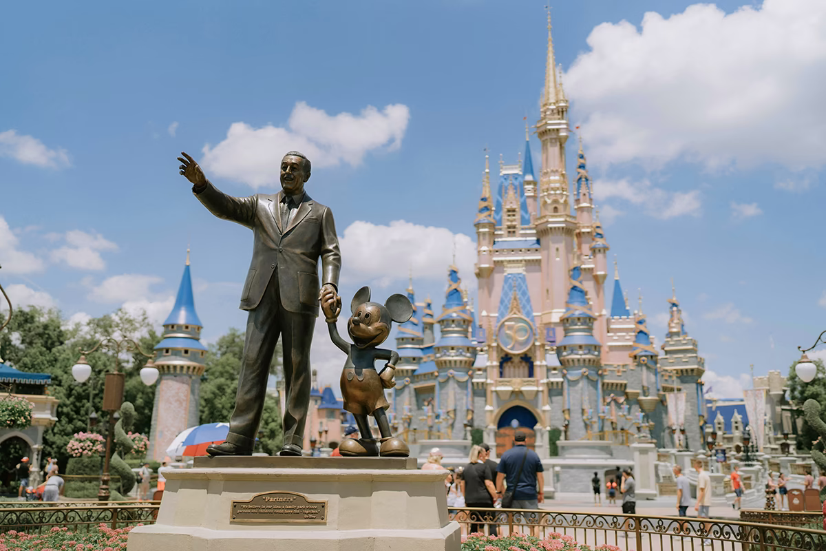 Statue of Walt Disney holding hands with Mickey Mouse in front of Cinderella Castle at a Disney theme park.