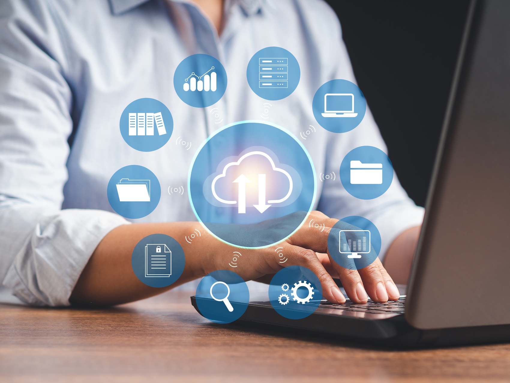Man sitting at a desk with floating icons above him representing cloud services like storage, computing, and networking.