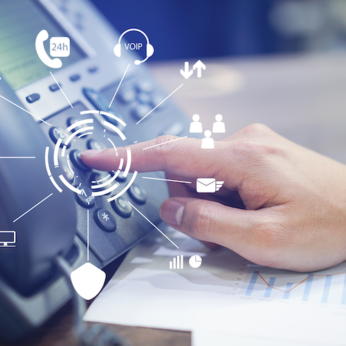 A person’s hand pressing a button on a telephone in an office setting.