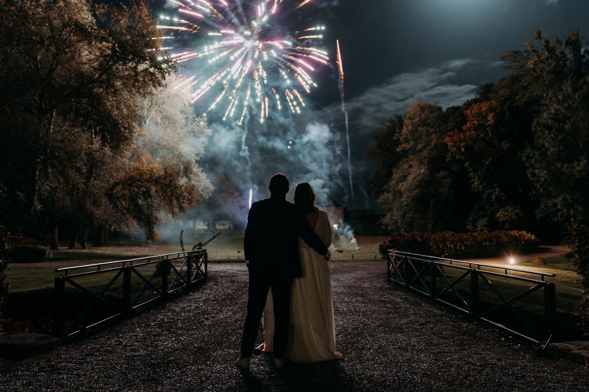 Feux d'artifice mariage - JSE Events
Les mariés regardent les feux d'artifice illuminer le ciel nocturne dans un jardin.