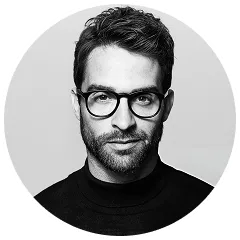 Black and white portrait of a man with glasses, short hair, and a beard wearing a dark turtleneck.