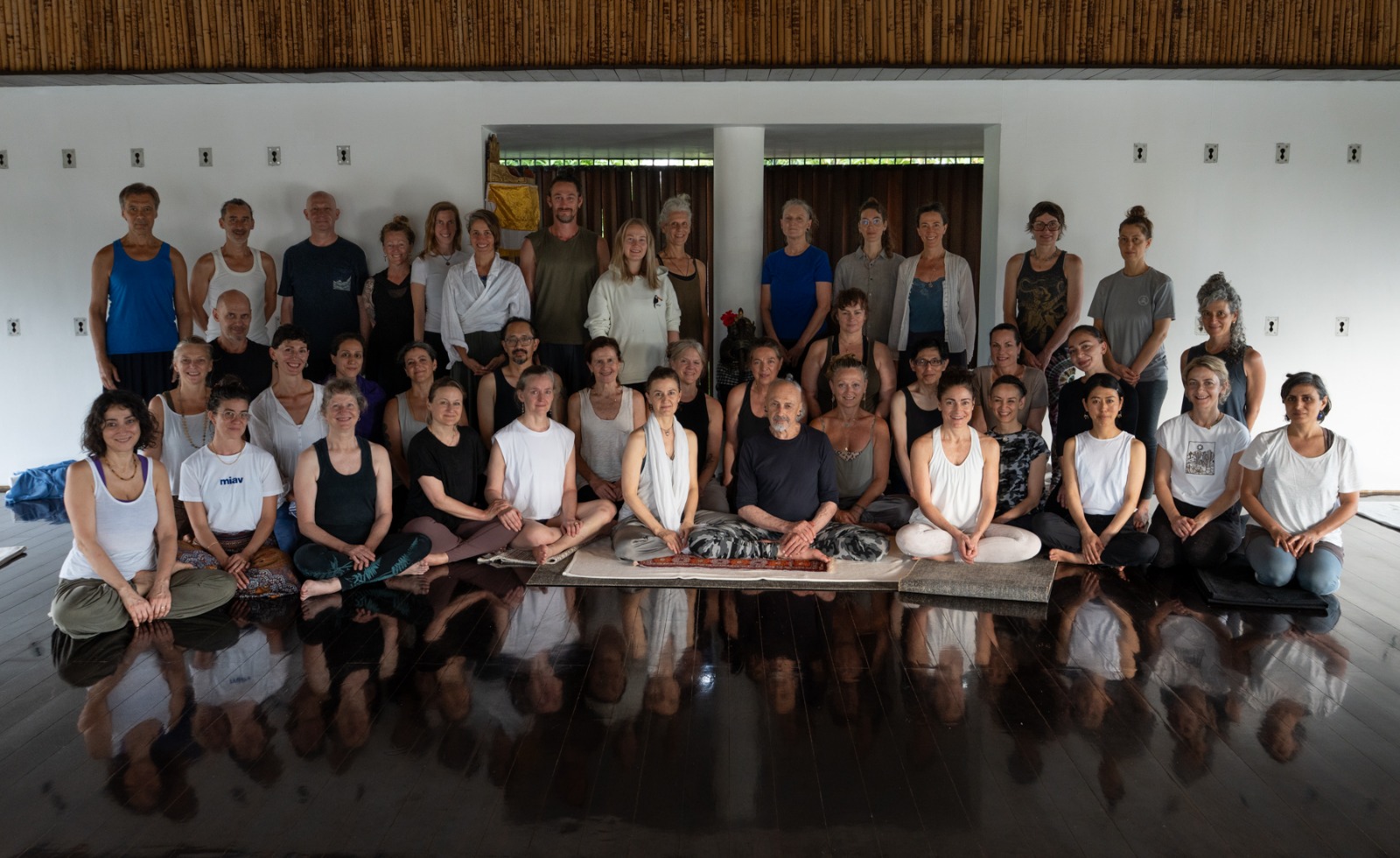 A group of Shadow Yoga teachers gathered in Bali; a Balinese statue representing the connection between human and divine forms; palm fronds against a blue sky
