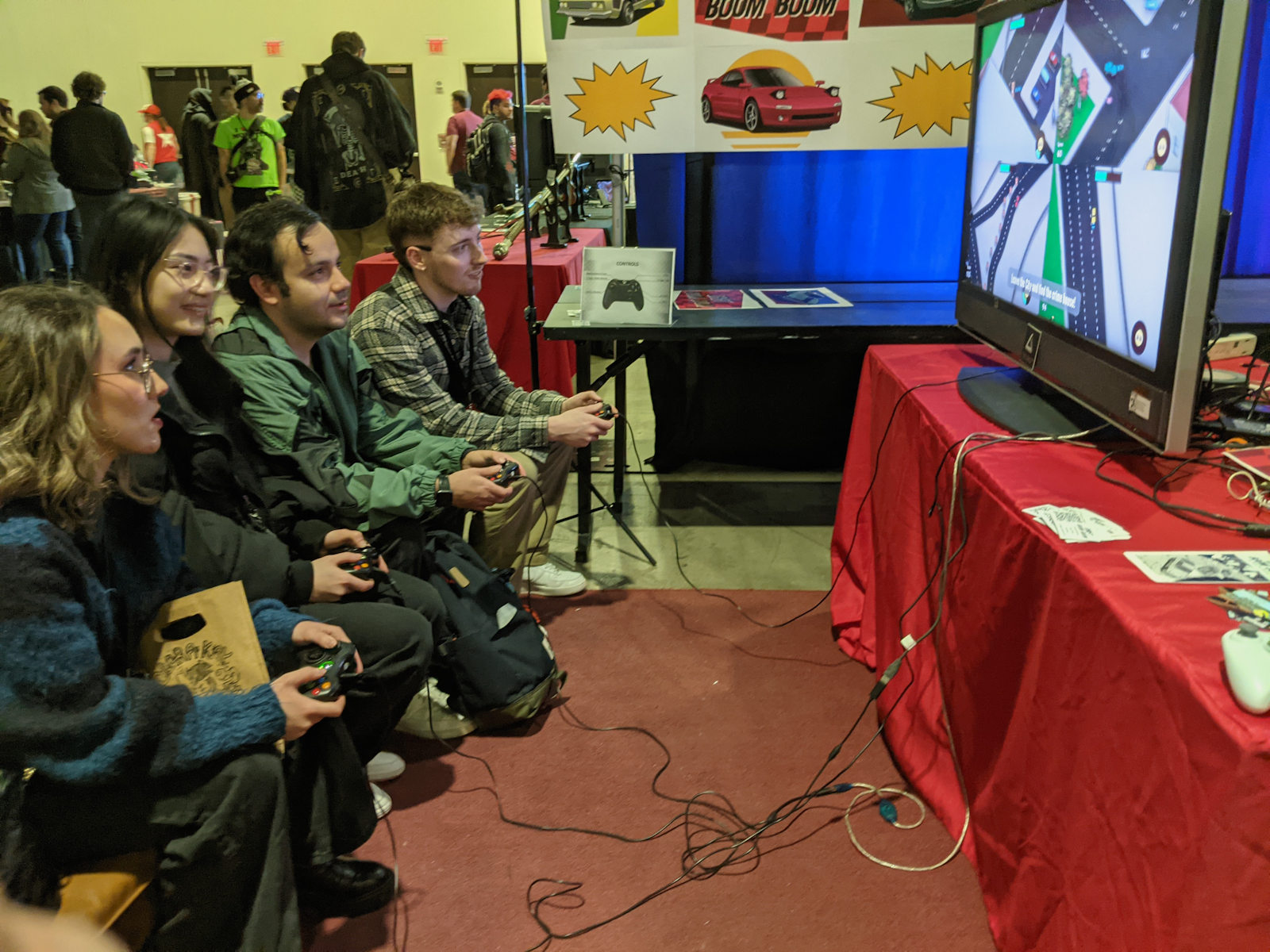 Four people crowded on a couch, enjoying DRIFT BOOM BOOM at a busy convention.