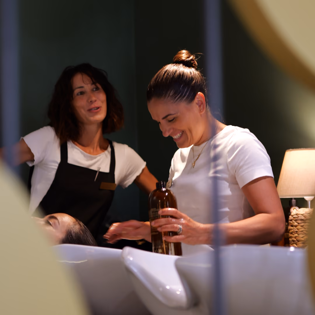 Una parrucchiera del salone Gala sorride mentre applica lo shampoo a una cliente nella zona lavaggio.