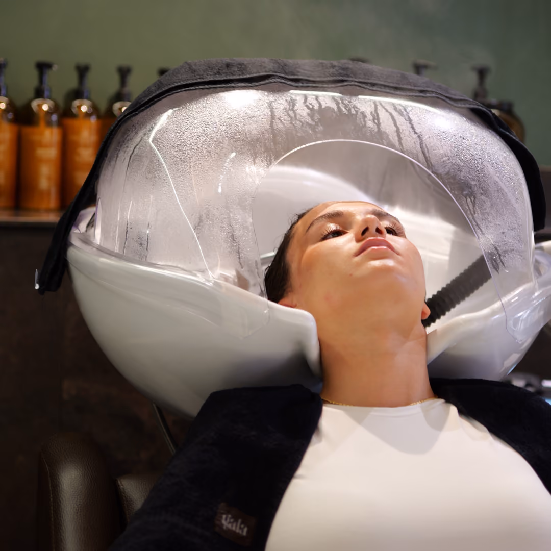 Cliente del salone Gala rilassata mentre si sottopone a un trattamento spa per capelli con vapore.