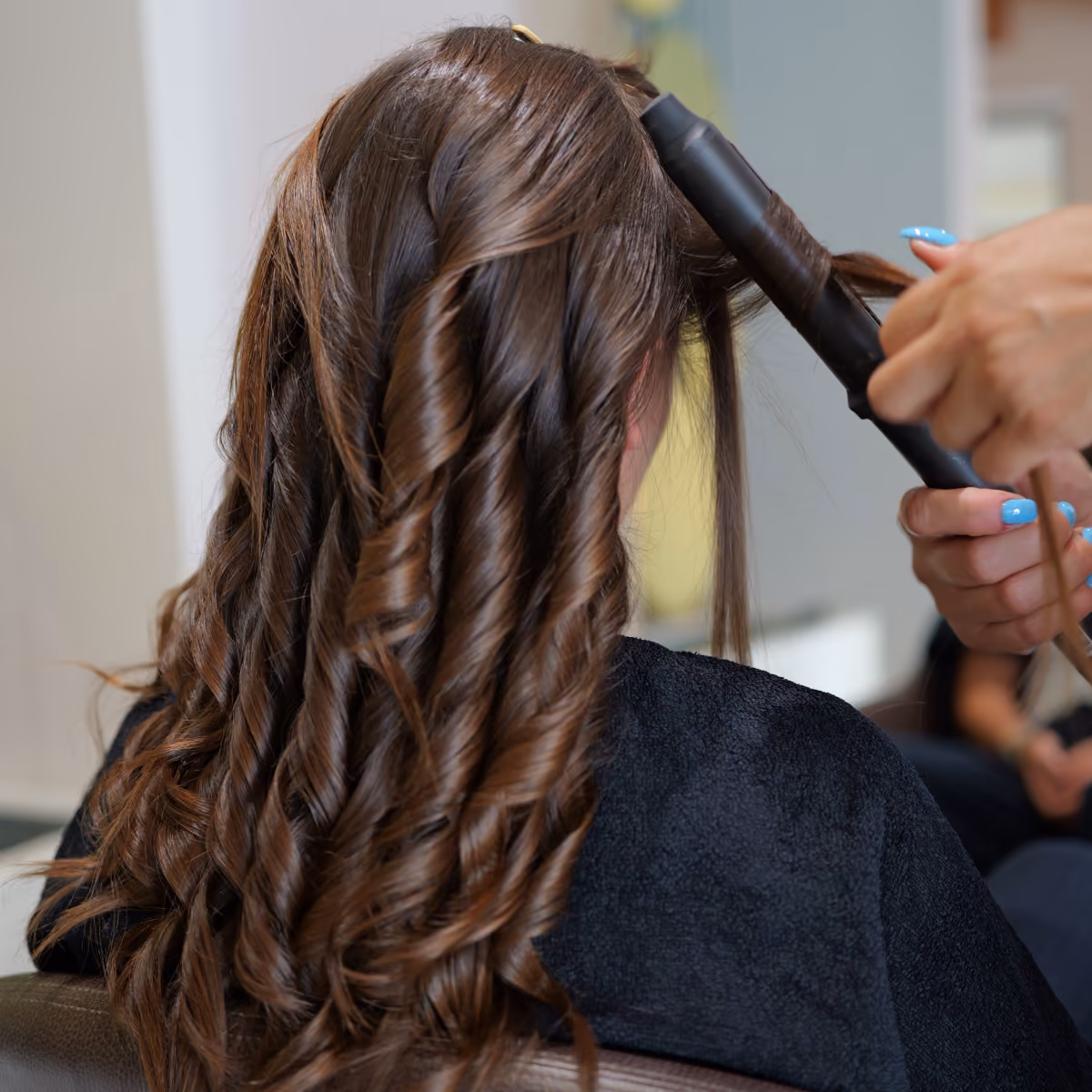 Primo piano delle mani di una stylist del salone Gala che usa un ferro arricciacapelli professionale per creare boccoli morbidi e definiti su lunghi capelli castani.