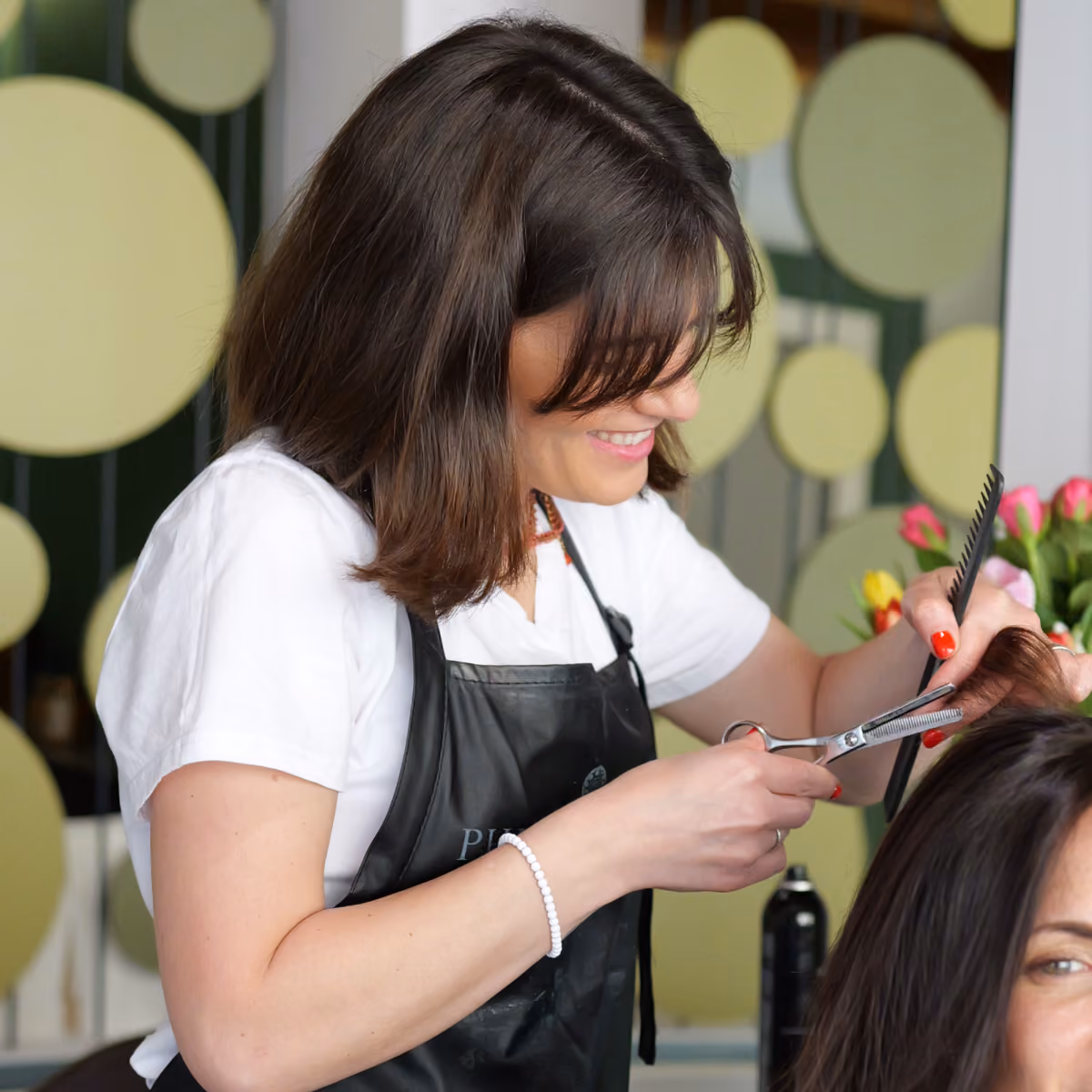 Stylist del salone Gala sorridente mentre esegue con precisione un taglio capelli usando forbici professionali e un pettine su una cliente.