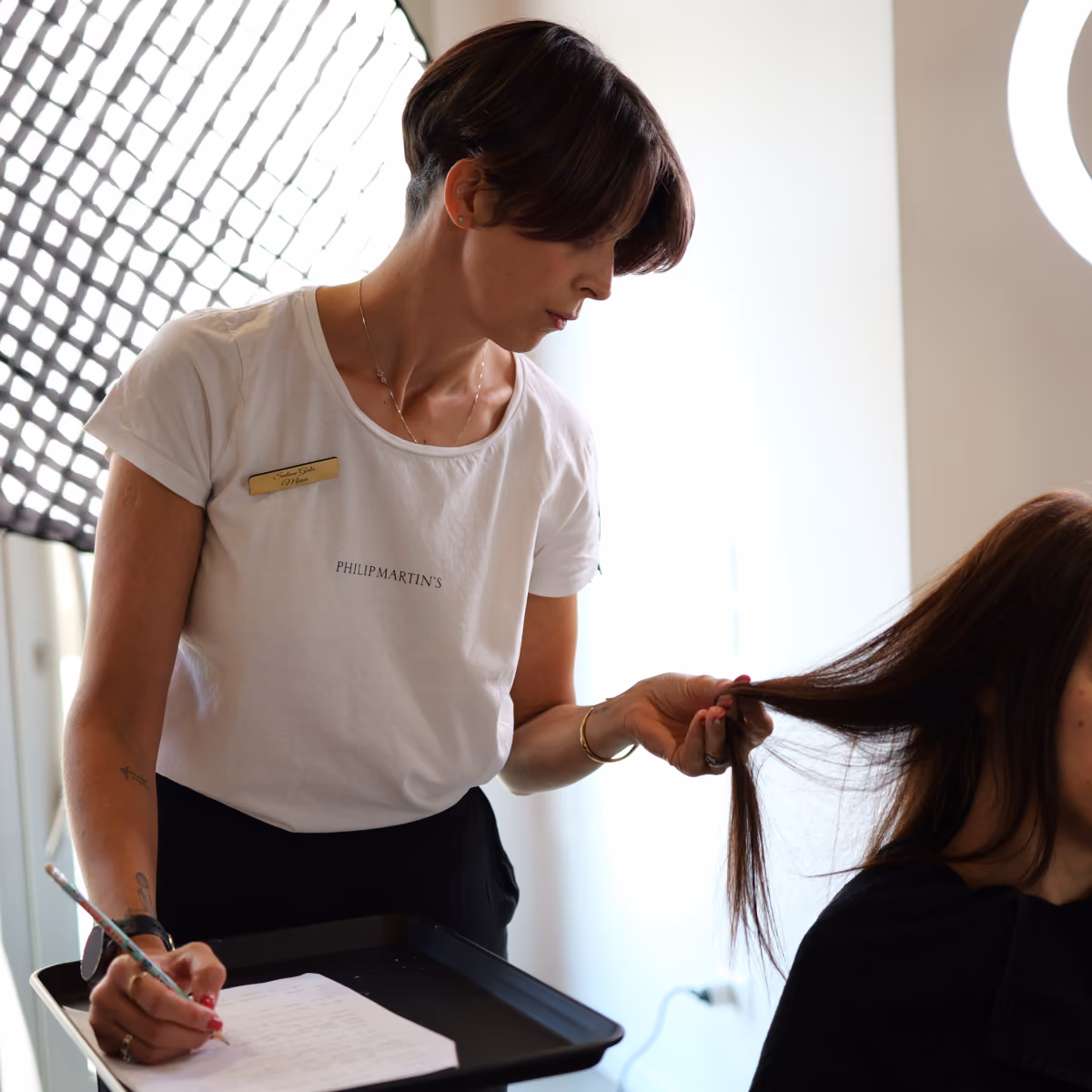 Stylist del salone Gala con maglietta Philip Martin's mentre esegue una consulenza personalizzata, analizzando i capelli della cliente e prendendo appunti su una scheda.