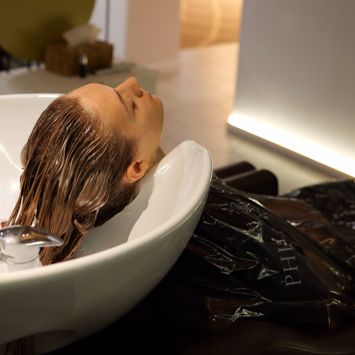 Cliente del salone Gala rilassata con gli occhi chiusi mentre si gode un momento di pausa e benessere durante il lavaggio dei capelli.