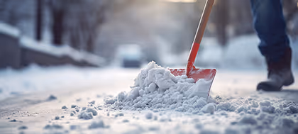 Person schaufelt Schnee auf einem verschneiten Weg bei gedämpftem Tageslicht.