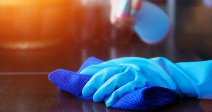 Hand mit blauem Handschuh wischt eine Oberfläche mit blauem Tuch bei Sonnenlicht.