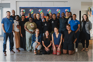 Group of diverse people posing and smiling indoors in front of a blue banner.