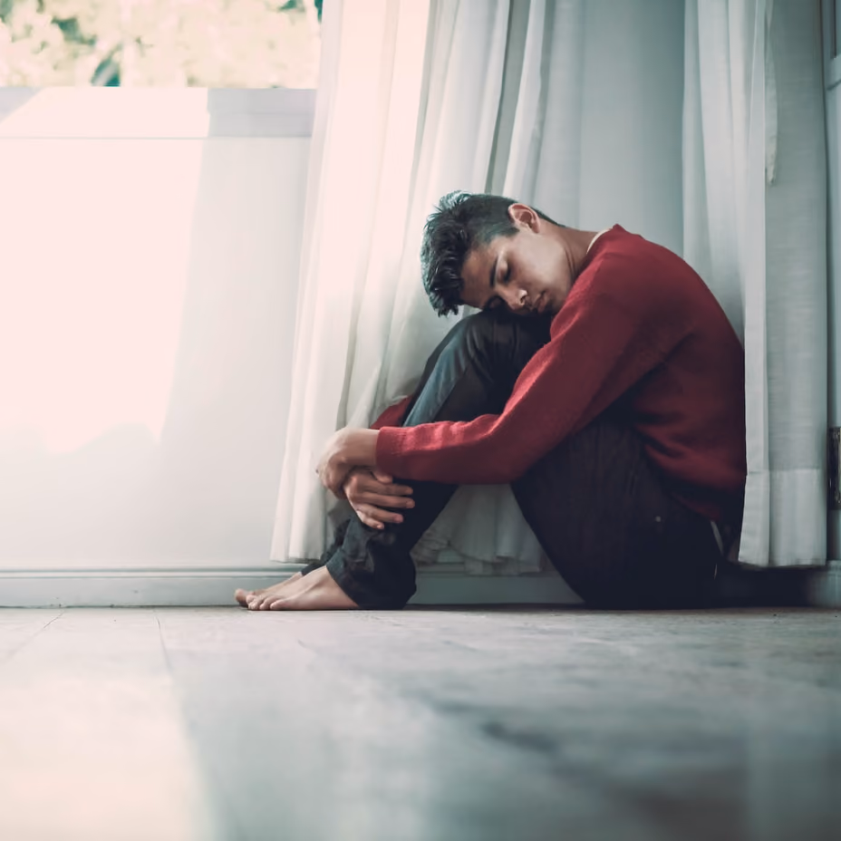 Young male resting his head on his legs as he struggles with emotion.