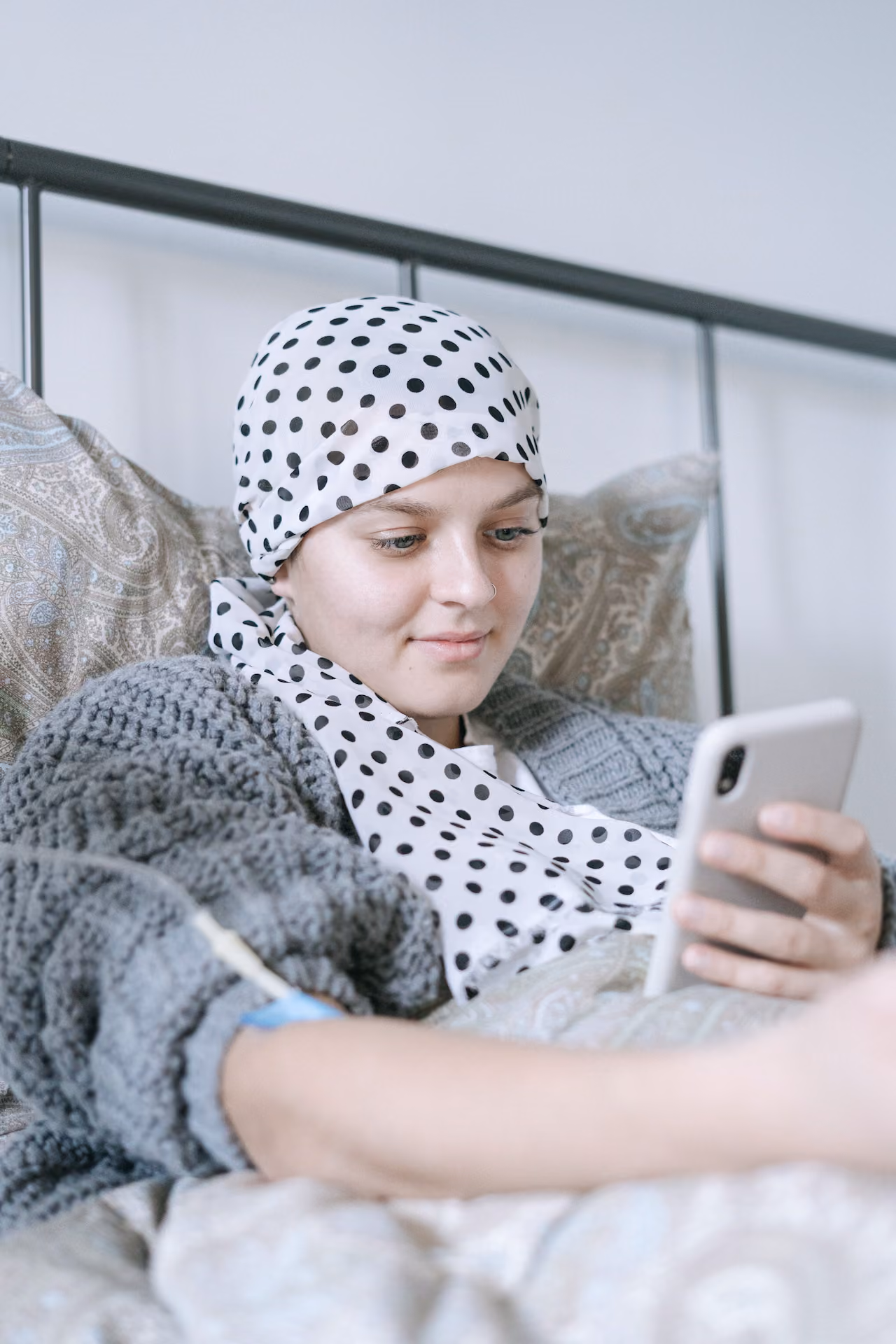Young female cancer patient smiling at her phone in bed.