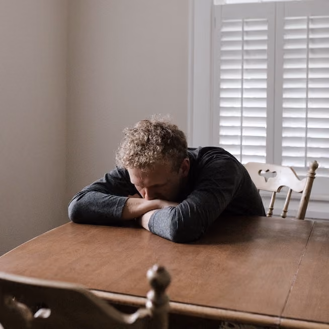 Young man resting his head on his arms at the dining table as he deals with intense emotions.