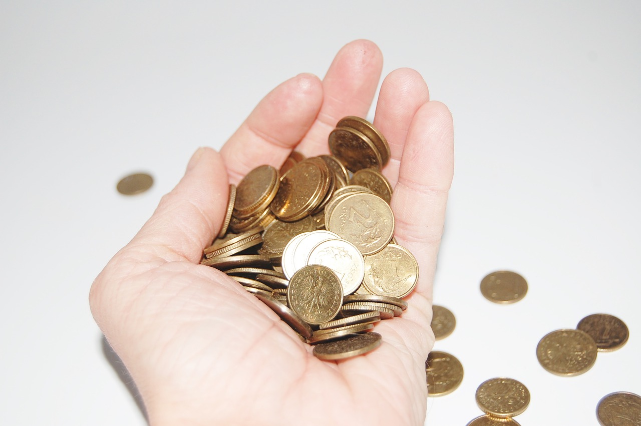 A hand holding a collection of coins, some spilling out onto the white tabletop below.